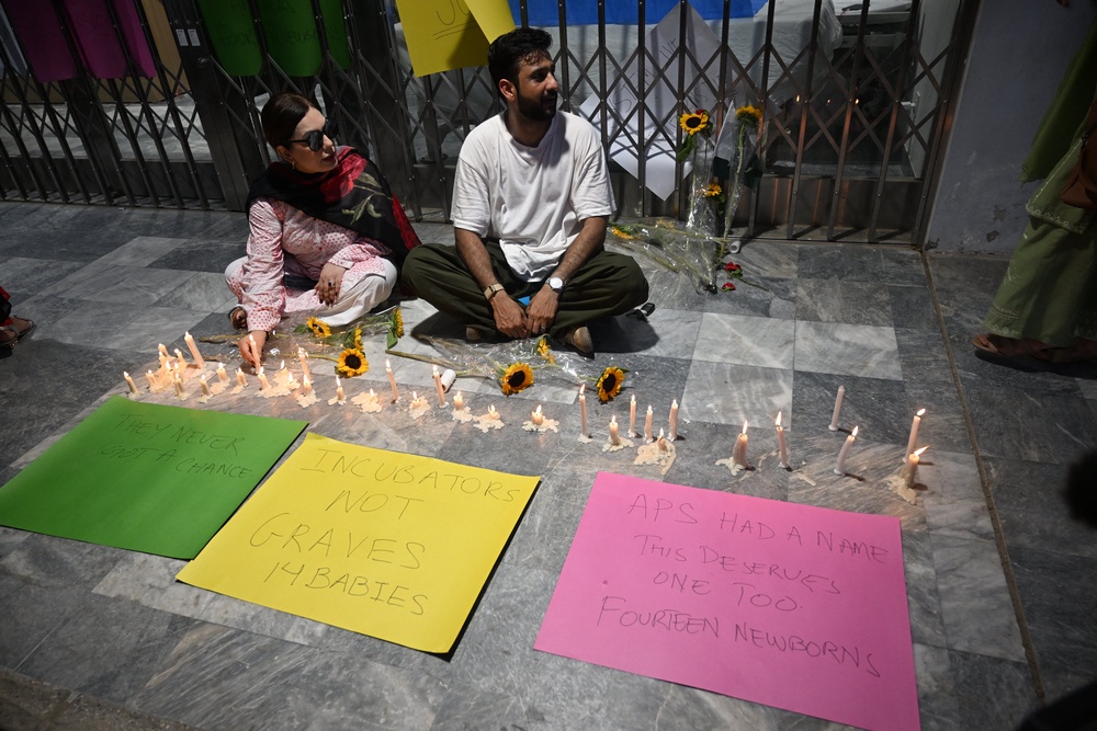 Activists light candles next to flowers placed outside the Mother and Child Health ward to protest against the death of infants in a fire at the Pakistan Institute of Medical Sciences (PIMS) Hospital in Islamabad on August 27, 2026 (AFP/Getty)
