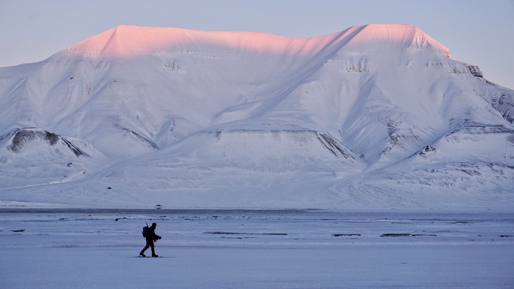 A skier with his rifle on his back makes his way on accross the snow-covered landscape with sun-kissed Hiorthfjellet mountain in the background on February 18, 2026 at Longyearbyen on the Norwegian archipelago of Svalbard (AFP/Getty)