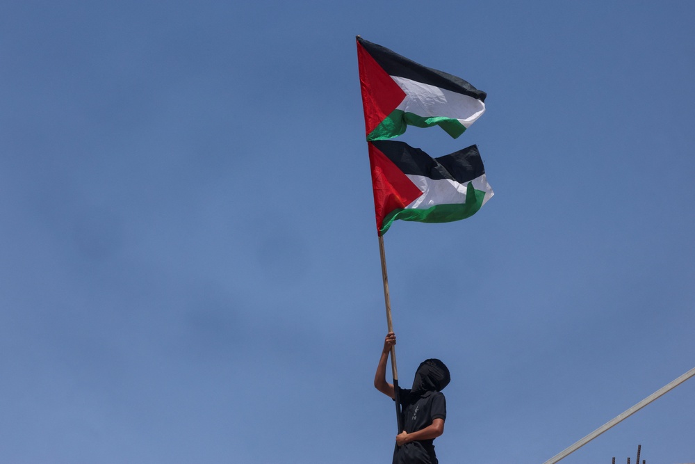 A person waves Palestinian flags during the funeral procession for two teenagers killed by Israelis at Al-Mughayyir village in occupied West Bank on 3 September 2026 (Reuters)