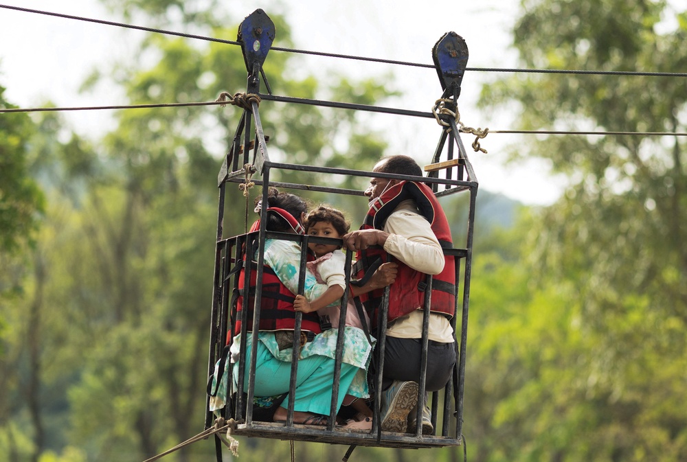 Madhu Sudan Sapkota, 50, Sangita Kunwar, 25, and her daughter Nekisha Rijal, 3, hold onto a cage on a makeshift zip line as they cross the Trishuli River from Koloni following deadly flash floods (Reuters)