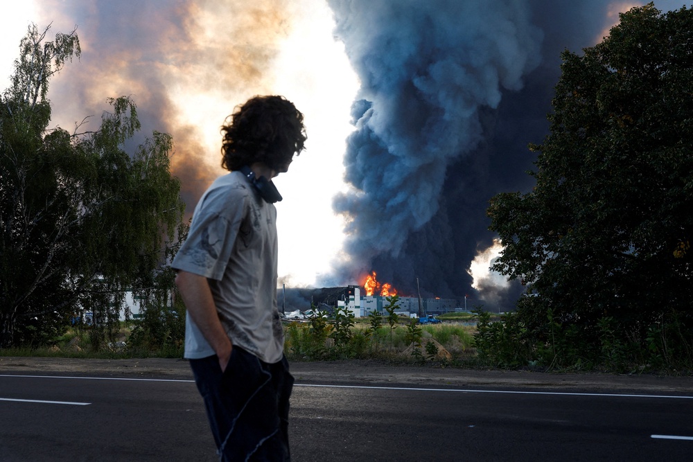 A man looks on as smoke rises over a warehouse, which was hit by a Russian drone strike, in Kyiv region (Reuters)