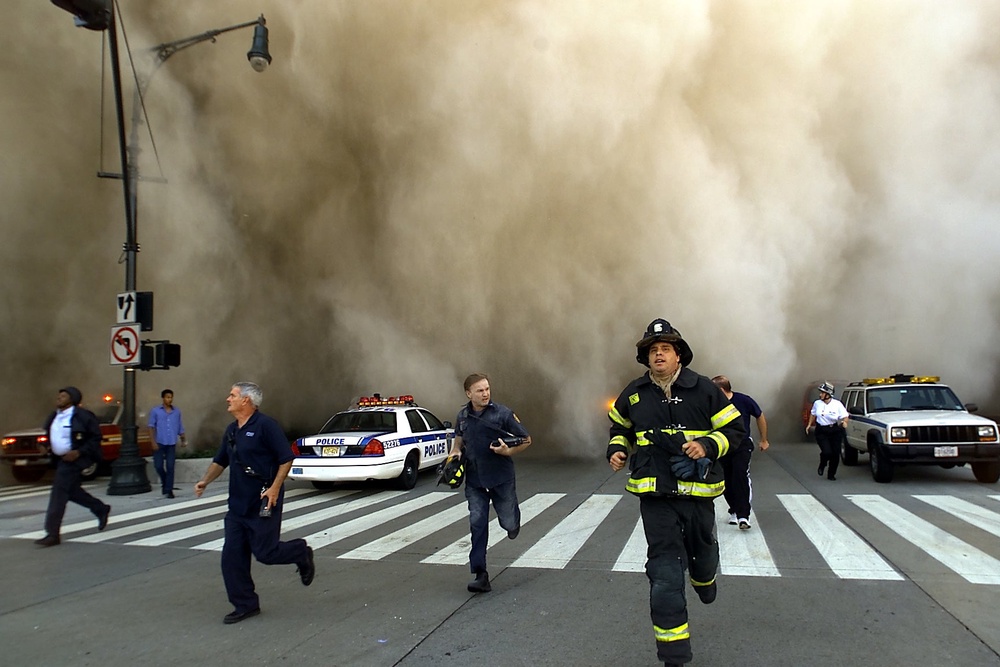 Policemen and firemen run away from the huge dust cloud caused as the World Trade Center's Tower One collapses (Getty)