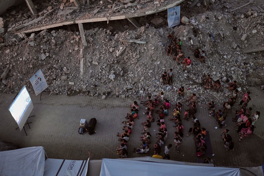 Displaced Palestinian children watch a movie amid the ruins of buildings destroyed by Israeli airstrikes (AP)