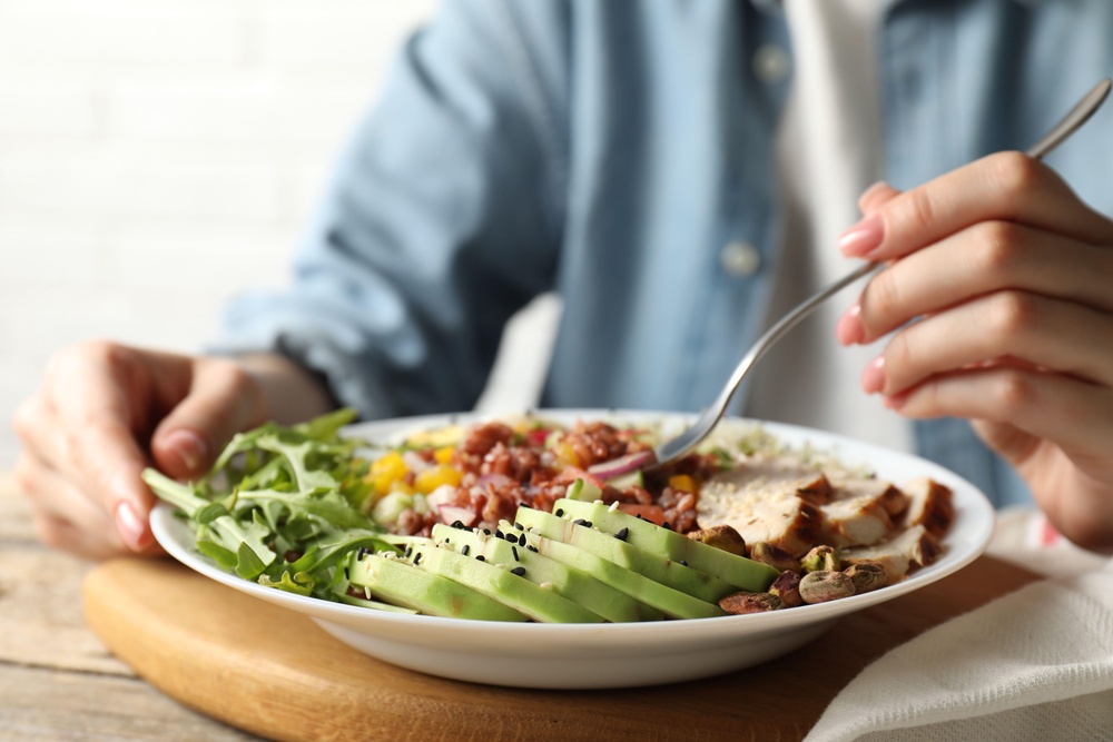 3B1YK75 Woman eating delicious salad with brown rice at wooden table, closeup