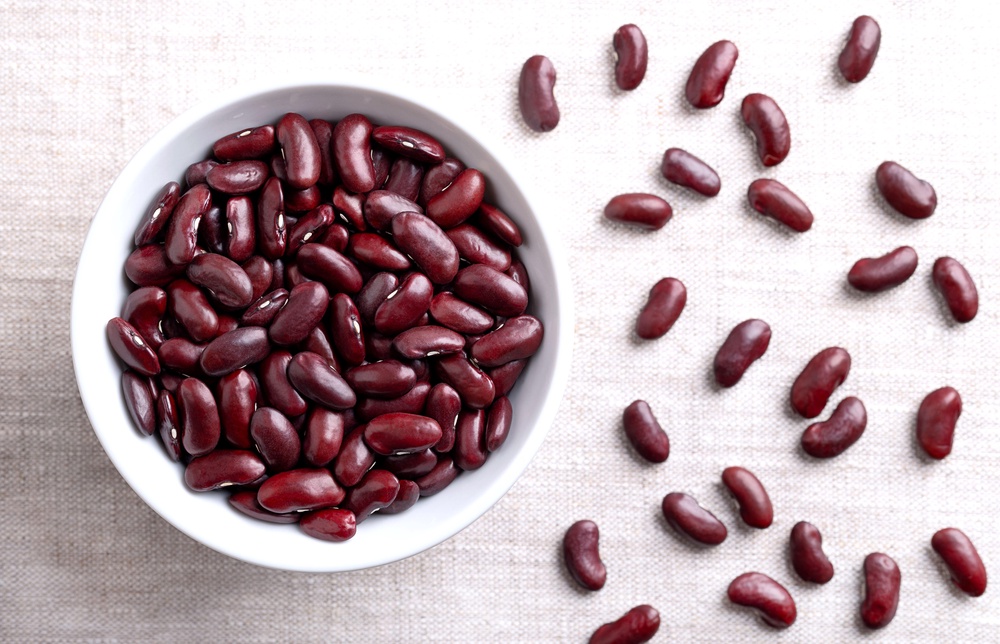 2YBWTX6 Dried kidney beans in a white bowl on linen fabric. Raw, uncooked, red common kidney beans, a variety of the bean Phaseolus vulgaris.