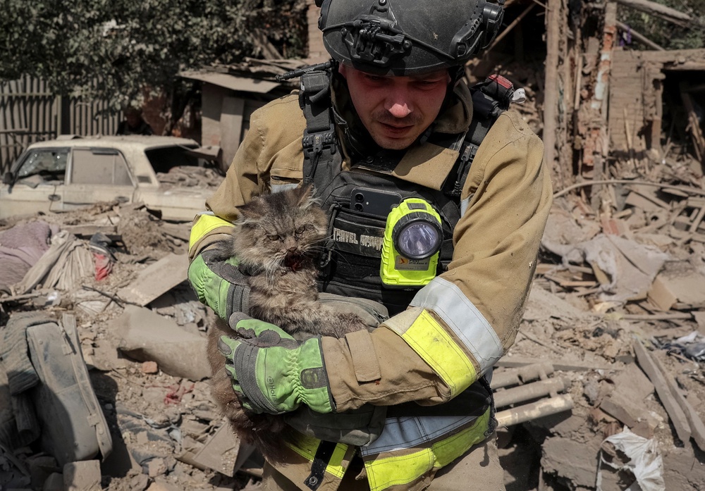A rescuer carries a cat found under debris at the site of a private house destroyed during a Russian air strike (Reuters)