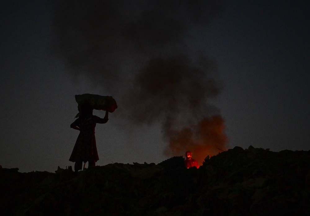 A woman carries a sack of garbage beside burning plastic wastage (Getty)