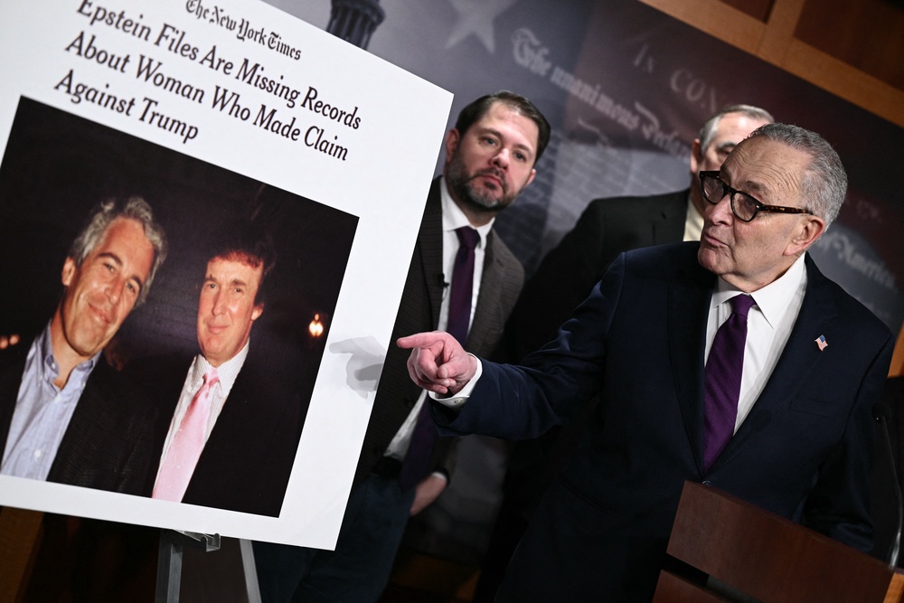 A sign showing a photo of President Donald Trump and Jeffrey Epstein is displayed by Senate Minority Leader Chuck Schumer during a press conference to announce oversight efforts on the files of convicted sex offender Epstein on February 26, 2026 (AFP/Getty)