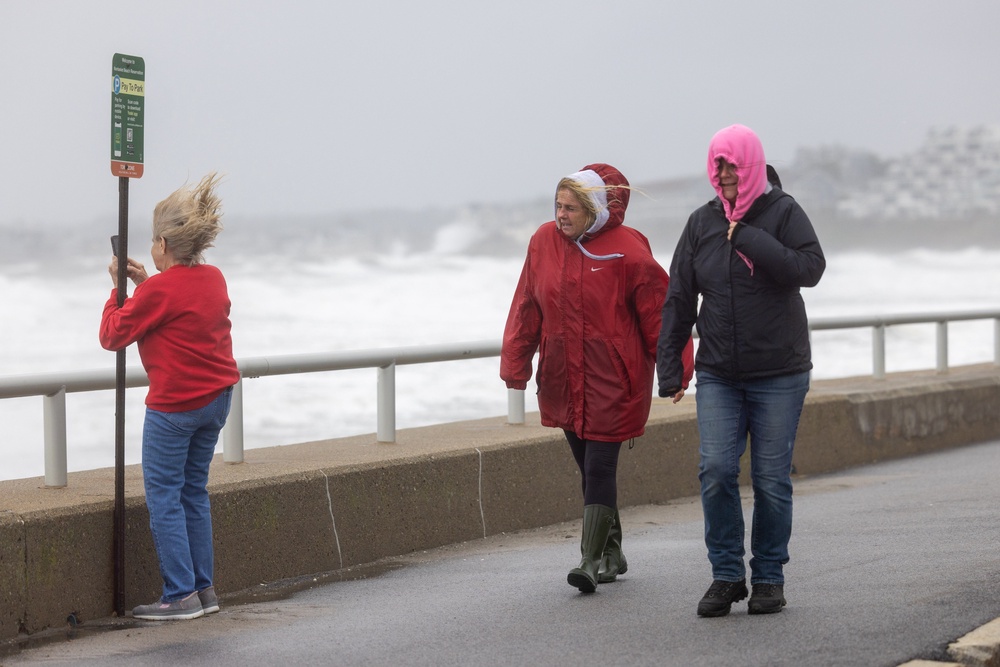People walk along Nantasket Beach as a woman takes photos of high surf on September 26, 2026 in Hull, Massachusetts (Getty Images)