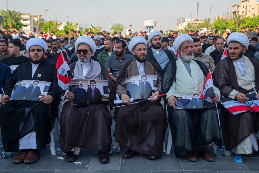 Shiite clerics sit with the portraits of Hezbollah's slain former chief Hassan Nasrallah and slain Iranian general Qassem Soleimani at the Tahrir Square in Baghdad (AFP/Getty)