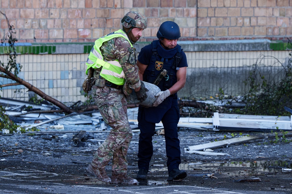 A police officer and a rescue worker carry an unexploded warhead from a Shahed drone out of a school damaged by a Russian strike on Kyiv, Ukraine, 1 Oct 2026 (AP)