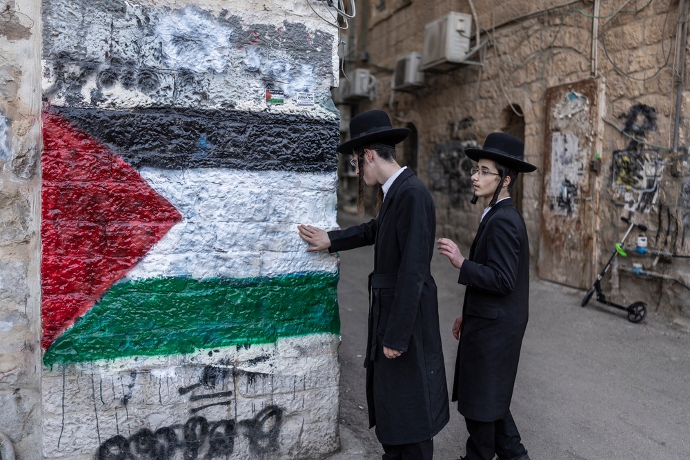 Members of the Neturei Karta, an international organisation of anti-Zionist Orthodox Jews, stand next to a mural depicting the Palestinian flag during a protest against the State of Israel, which they believe should not exist before the coming of the messiah, in the Jerusalem neighbourhood of Mea Shearim on April 22, 2026 (AFP/Getty)