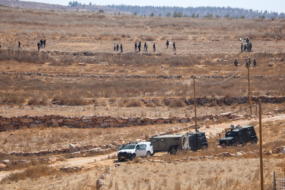 Groups of people are spread across a rocky hillside above several Israeli military vehicles in Wadi al-Rakhim, south of Yatta, occupied West Bank, on October 7, 2026. (AFP/Getty)
