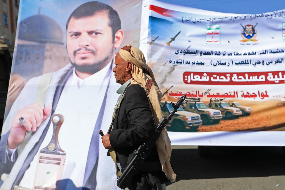 A fighter loyal to the Houthi authorities walks past a poster bearing a picture of his group’s leader, Abdul-Malik al-Houthi, during a rally to recruit more fighters (AFP/Getty)