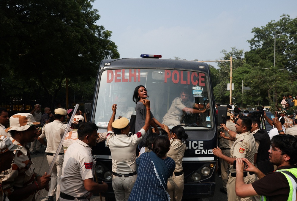 A protester tries to stop a police bus carrying detained protesters in Delhi (Reuters)