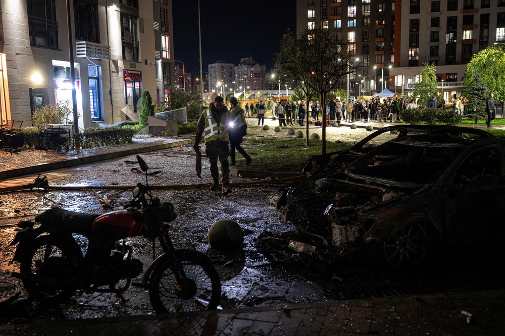 Local residents watch a Ukrainian police officers working by wreckage cars in front of a high-rise residential building damaged following a Russian drone attack, in Kyiv (AFP/Getty)