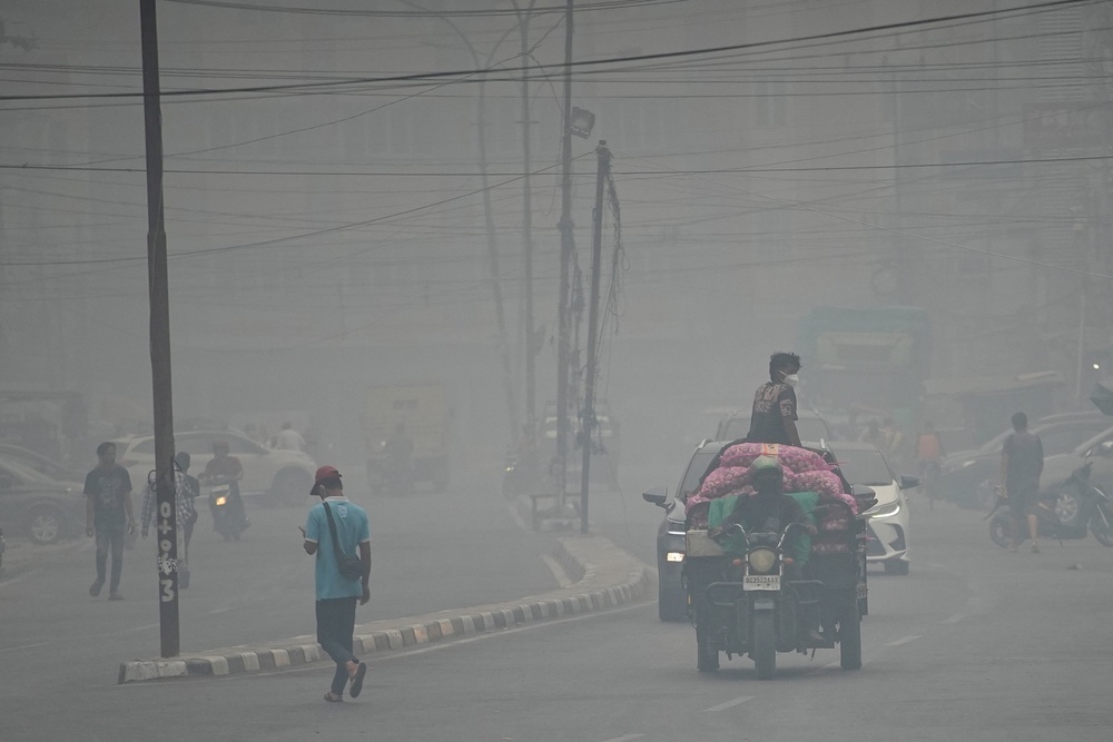 People wearing protective masks ride on a three-wheeled vehicle through a road as haze from wildfires shrouds the area in Palembang, South Sumatra province, Indonesia, October 15, 2026 (Reuters)