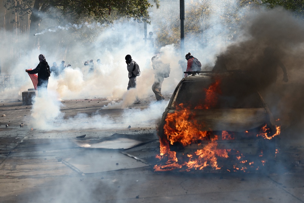 Protesters stand next to a burning car amid clashes during a demonstration at the Place de la Republique in Paris (Reuters)