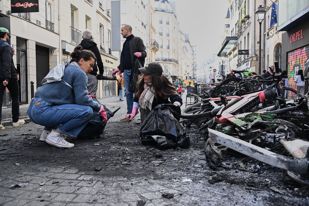 People clean up debris in a street next to burned bicycles in Paris (AP)