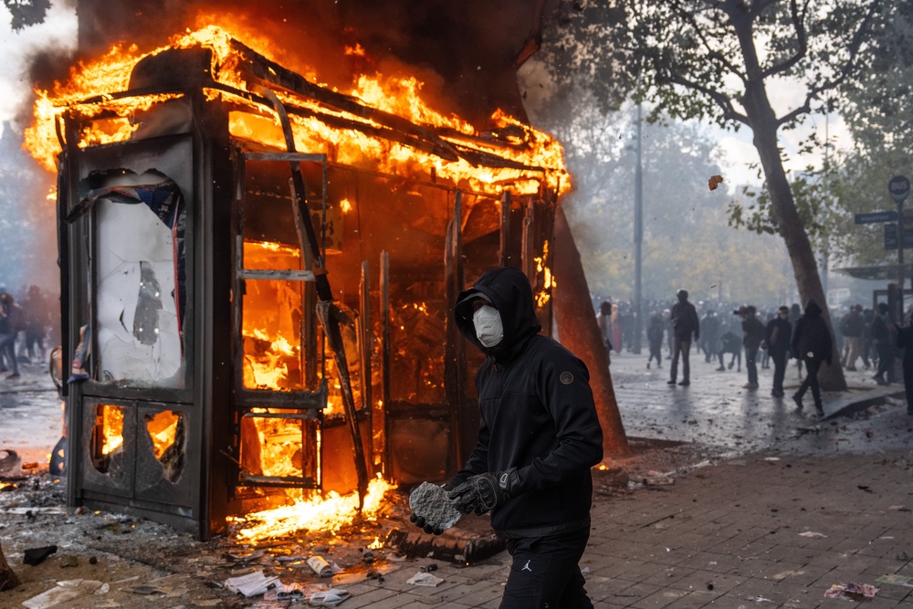 A protester holds a rock to throw at police as a kiosk burns during a demonstration at Place de la République (Getty)