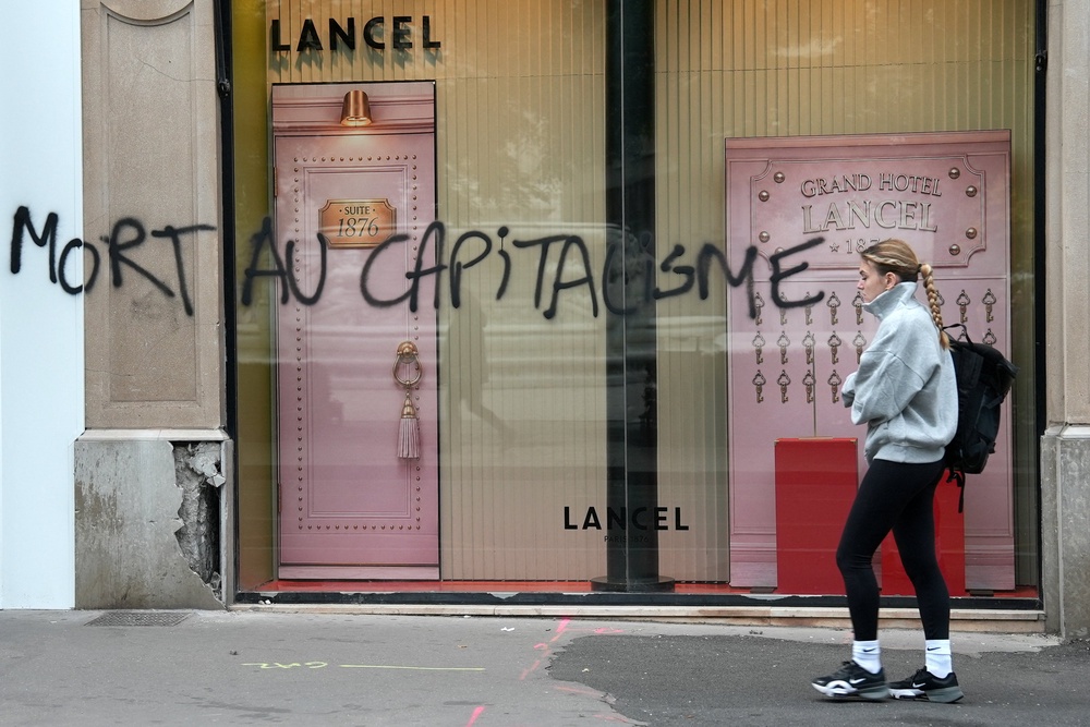 A woman walks past a Lancel store that was vandalised during clashes that erupted during a national day of demonstrations against the cost of living and rising fuel prices, in Lyon, France, October 19, 2026. The graffiti on the store window reads 