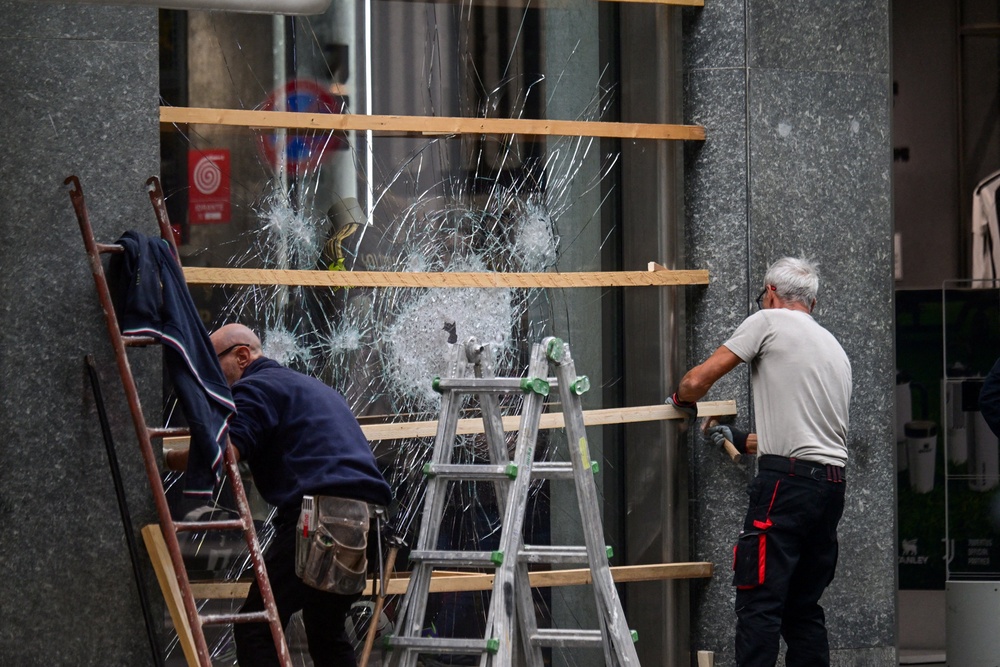Workers secure a shattered shop window with wooden boards following clashes between police and protesters (REUTERS)