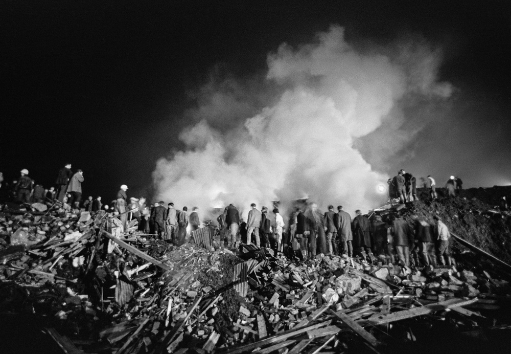 Rescue workers stand on a mound of rubble amid smoke at night in the aftermath of the Aberfan Disaster, (Getty Images)