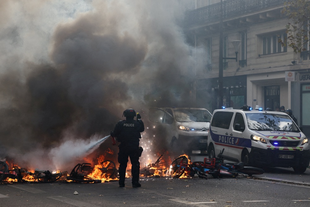 A French police officer extinguish burning bicycles during a demonstration against the cost of living and rising fuel prices in Paris as part of nationwide protests (Reuters)