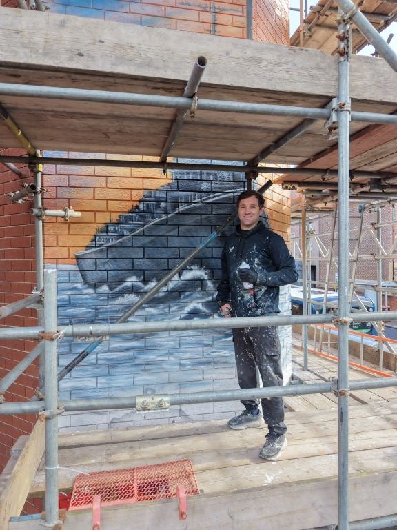 Neil Keating, at work on a mural on the side of Ilkeston Town Hall i (PA)
