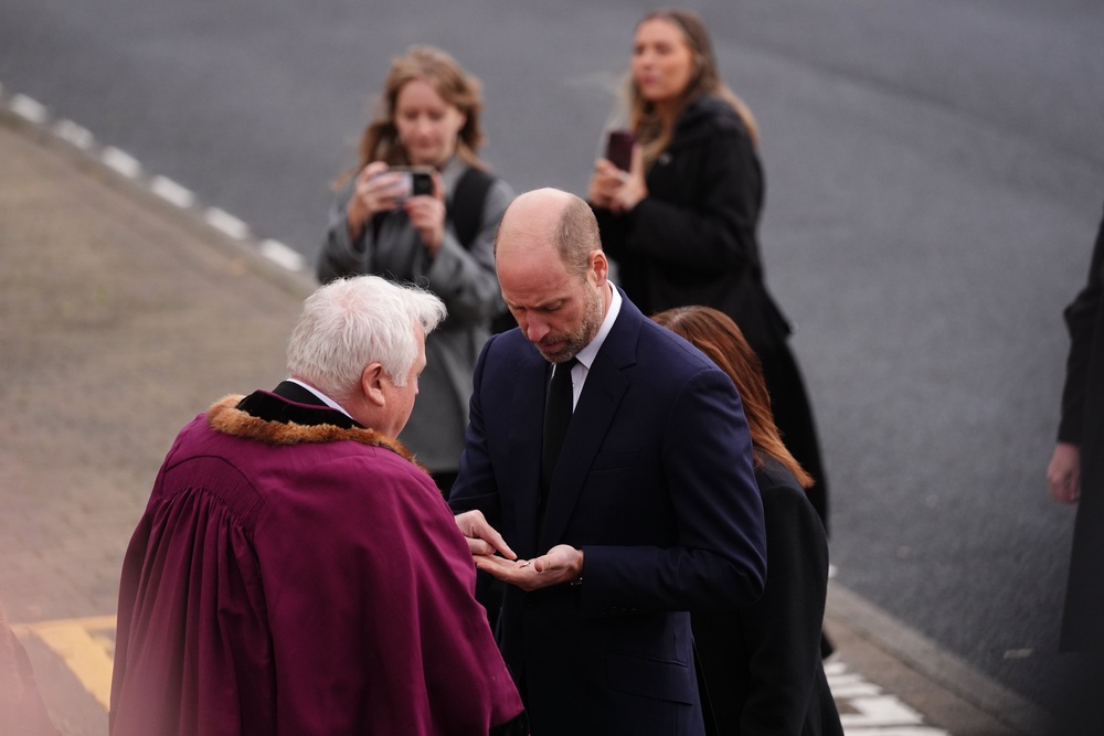 The Prince of Wales looking at a 60th anniversary pin displaying a clock face on it with the time the coal tip collapsed, which he was asked to forward on to the King, as he arrived at Aberfan and Merthyr Vale Community Centre (Jacob King/PA) (PA Wire)