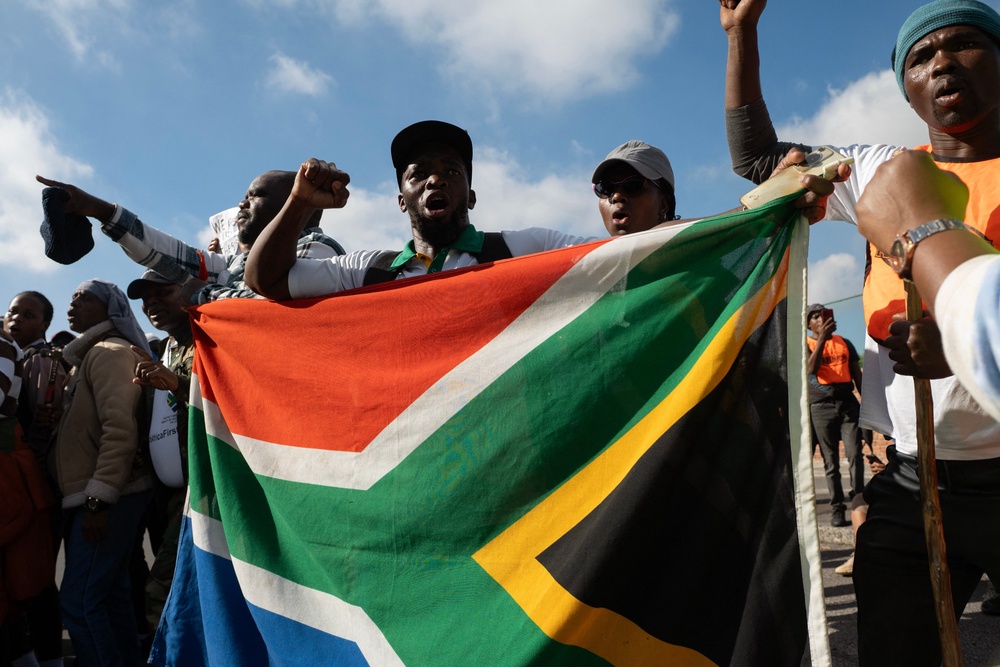 Demonstrators hold a South African flag as they chant slogans during a protest against undocumented migrants organised by the March and March and Operation Dudula groups in Cape Town on May 23, 2026 (AFP via Getty Images)