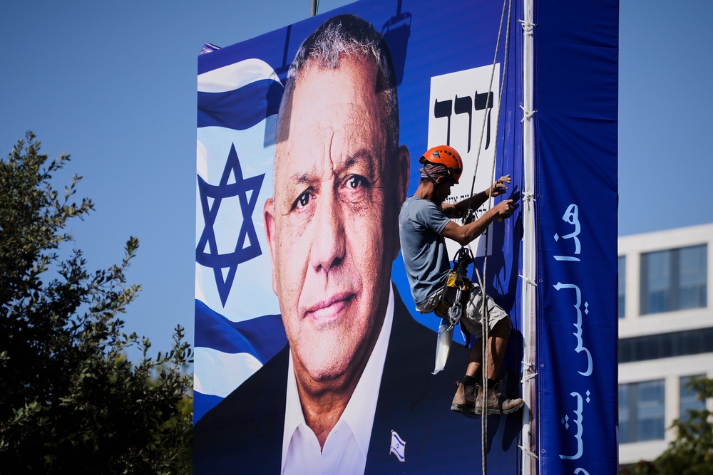 A worker hangs a campaign billboard in Jerusalem featuring Gadi Eisenkot, leader of Yashar party, ahead of Israel’s general election (AP)