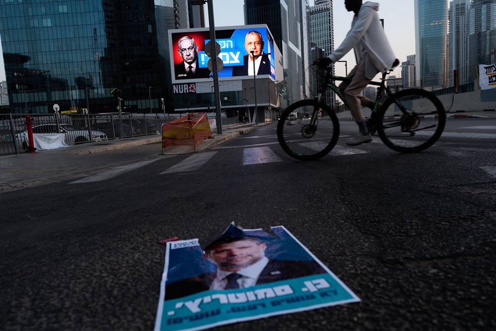 A cyclist passes a campaign billboard featuring Netanyahu, left, and his main rival, opposition candidate Gadi Eisenkot, with a message in Hebrew that reads ‘The race is tight’ (AP)