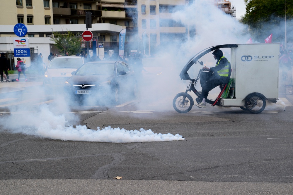 A car and a cyclist amid a cloud of tear gas and next to a fuming tear gas pellet in Lyon (AFP/Getty)