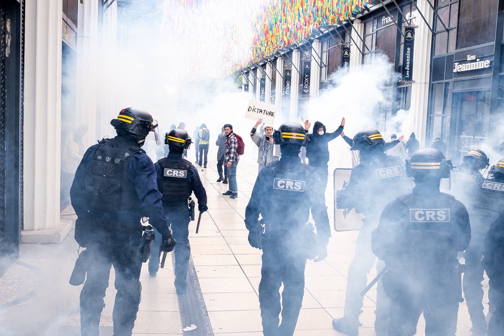 Man holding a sign denouncing dictatorship in front of French police officers in a smoke of tear gas and in front of Clemenceau square shops, Pau (AFP/Getty)