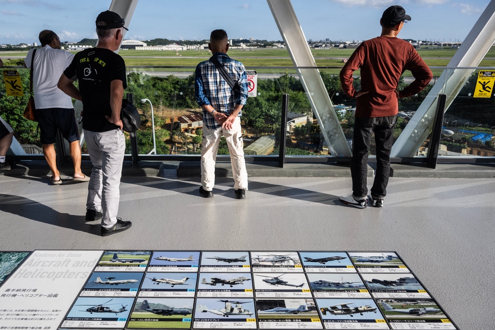 People watch the flight line near a poster showing the different kinds of aircraft next to Kadena Air Base in Kadena, Okinawa prefecture (AFP/Getty)
