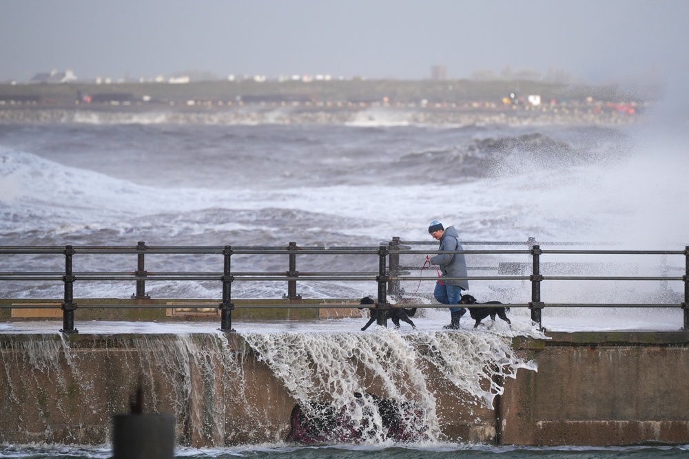 A person walks their dog along the sea wall as waves created by the high winds of Storm Boelo hit the sea wall at New Brighton promenade in Merseyside (Getty)