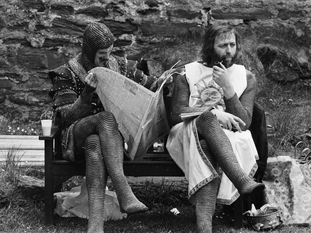 A chainmail-clad John Cleese reads a newspaper while Graham Chapman smokes a quiet pipe on the set of ‘Monty Python and the Holy Grail’ (Getty Images)