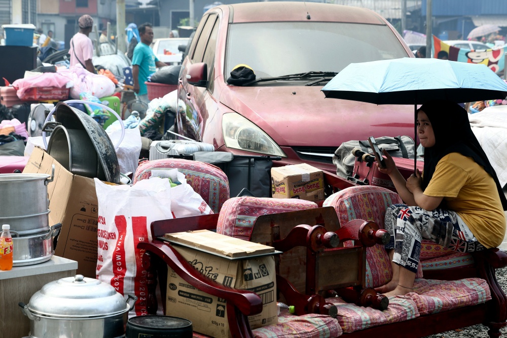 A woman sits among salvaged household belongings in an open area following a blaze at Kampung Bahagia in Sandakan April 19, 2026. — Bernama pic