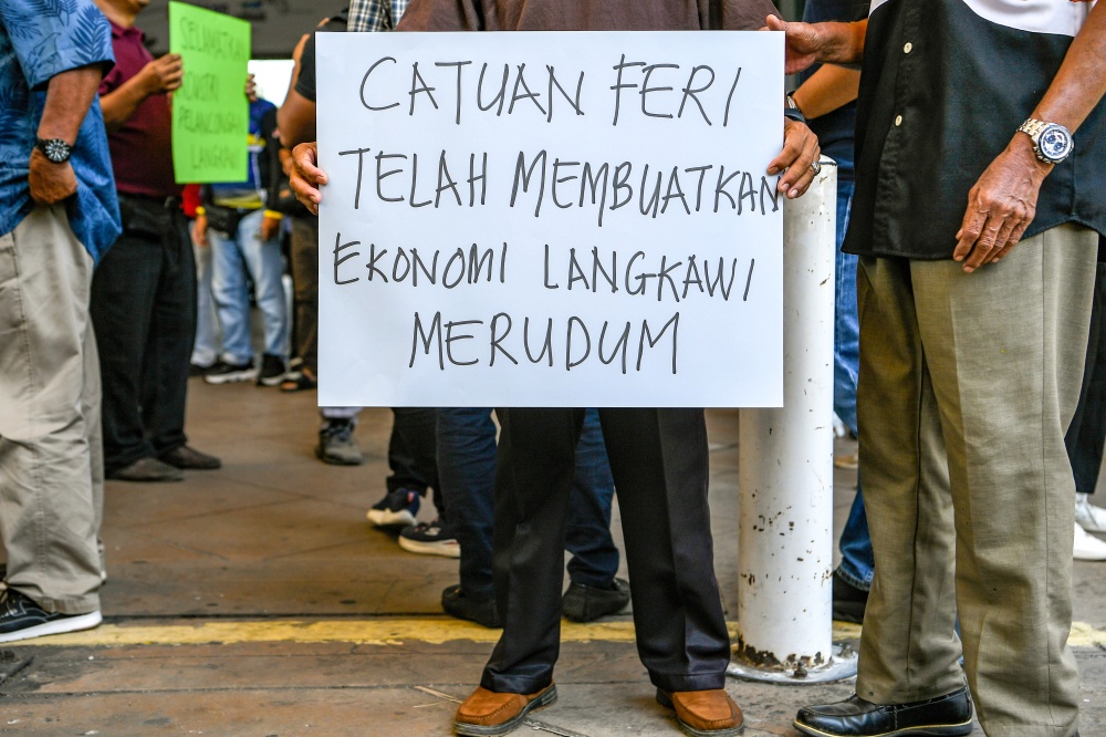 A demonstrator holds a placard that reads: ‘Ferry rationing has caused Langkawi’s economy to decline sharply’ during a rally in Kuah on April 19, 2026. — Bernama pic