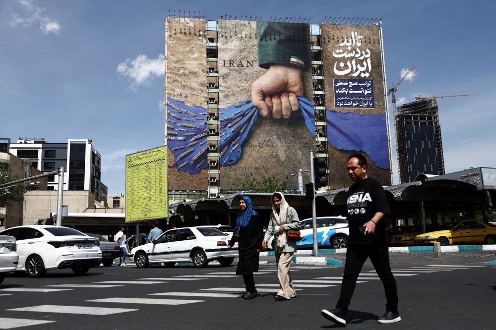 People walk past a billboard with a graphic design about the Strait of Hormuz on a building in Tehran on April 27, 2026. — Reuters pic