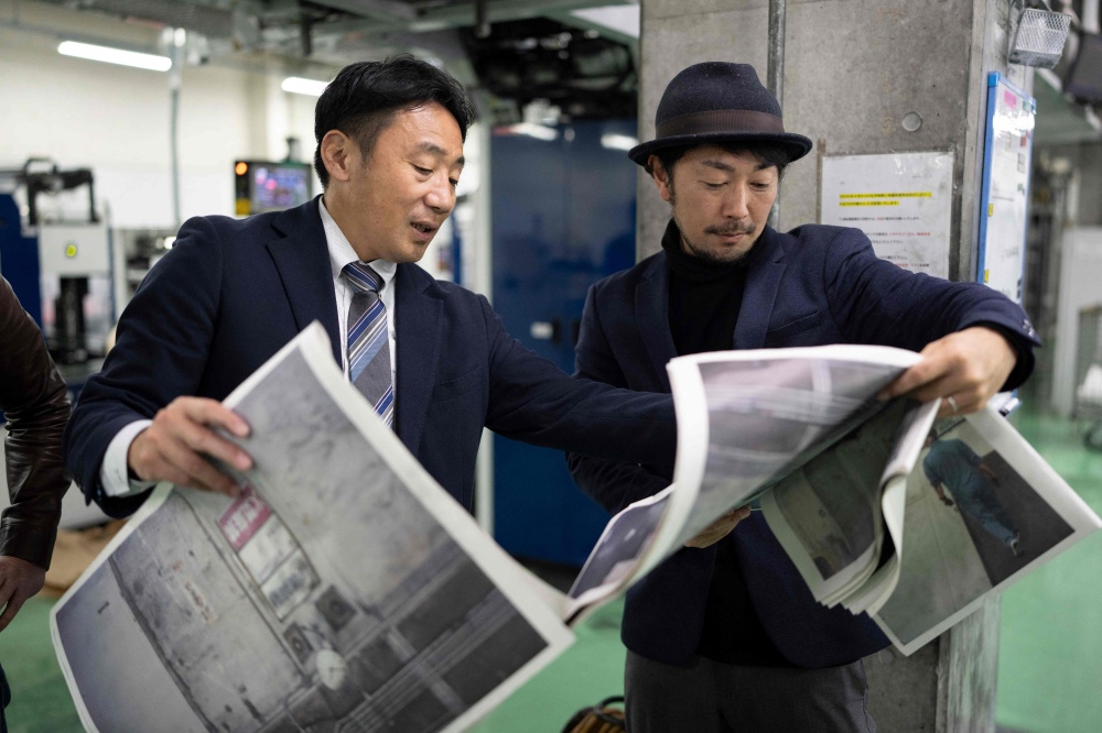 This picture taken on March 19, 2026 shows photographer Kazuma Obara (R) and a staff member inspecting the printing quality of his work titled “The Newspaper” at the Kyoto Shimbun factory in Kumiyama, Kyoto prefecture. Despite the decline of the publishing industry, self-publication and handmade 