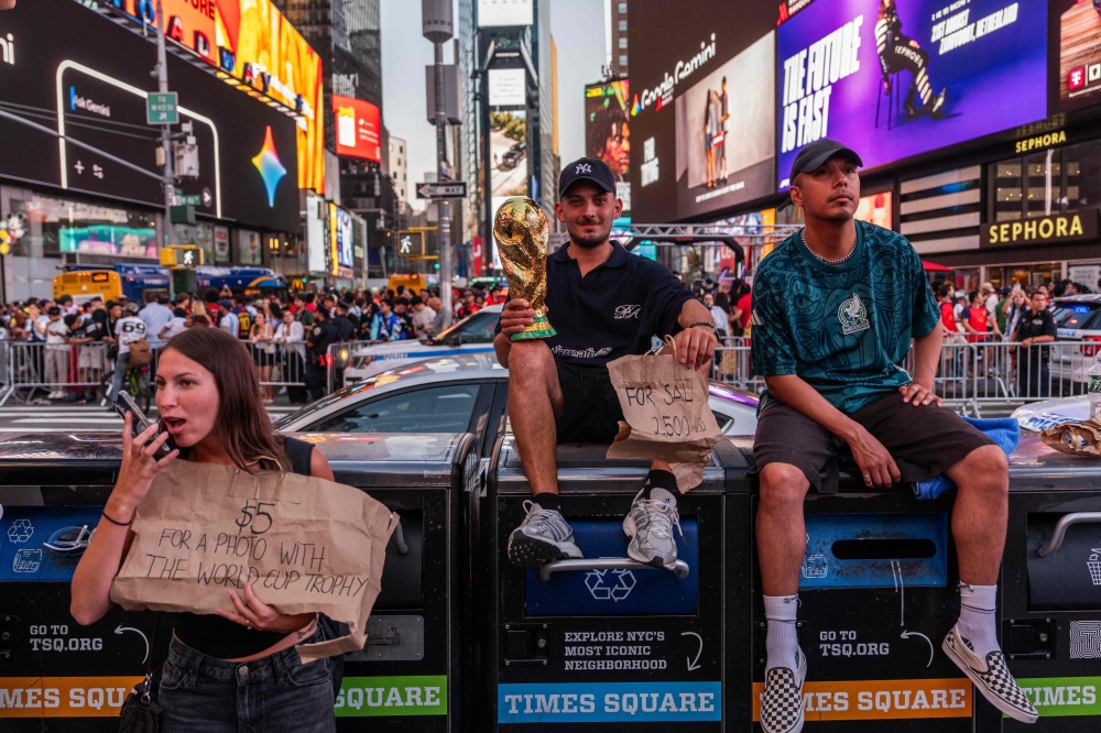 A tout holds a replica trophy for sale as people gather in Times Square after Spain defeated Argentina in the 2026 World Cup final. — Getty Images via AFP