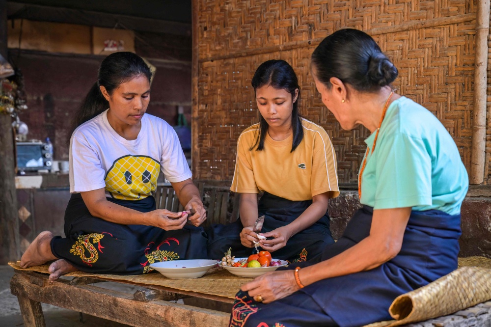 This photo taken on June 24, 2026 Rambu Margaretha (R), a maramba (noblewoman), looking on as two atas (slaves/servants) prepare ingredients for a meal at Kampung Raja Prailiu at Waingapu in East Sumba, East Nusa Tenggara. — AFP pic