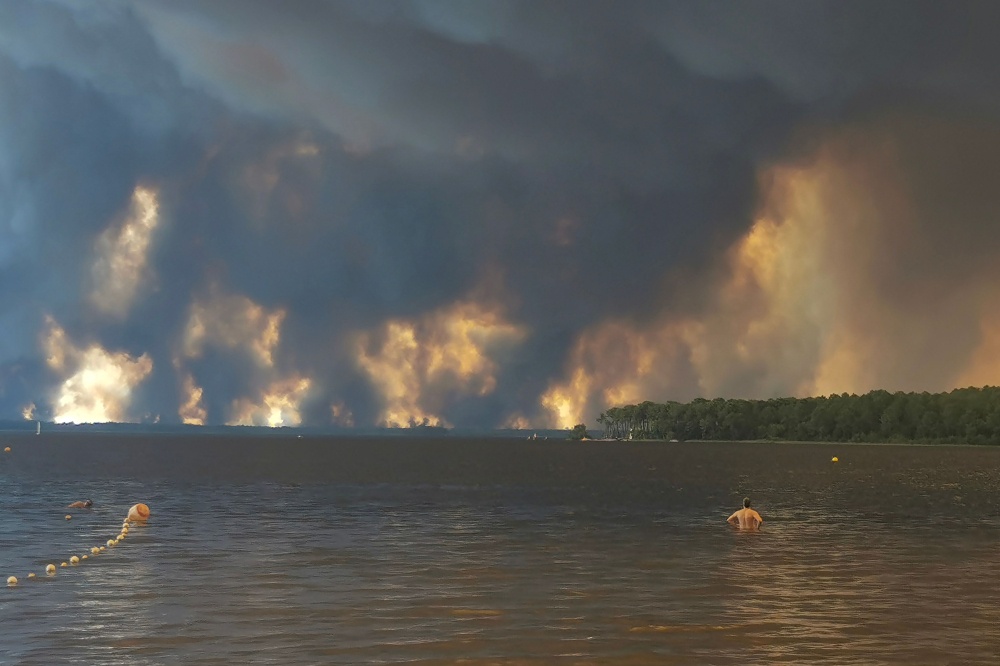 A beach goer stands in the ocean from the beach of Moutchic in Lacanau, southwestern France on July 24, 2026, as clouds of smoke rise into the sky from a wildfire. — AFP pic