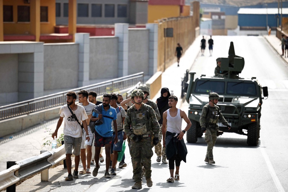 Spanish forces escort migrants to the Ceuta-Morocco border gate in the Spanish North African enclave of Ceuta August 1, 2026. — AFP pic 