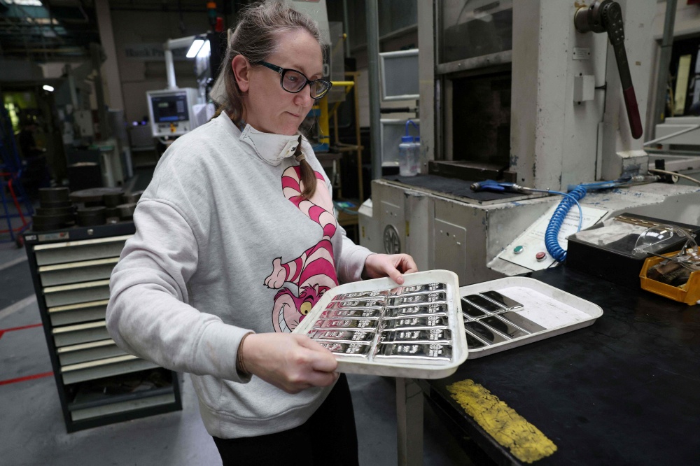 A worker removes silver bullion bars from a string tool at The Royal Mint in Llantrisant, south Wales on June 30, 2026. — AFP pic
