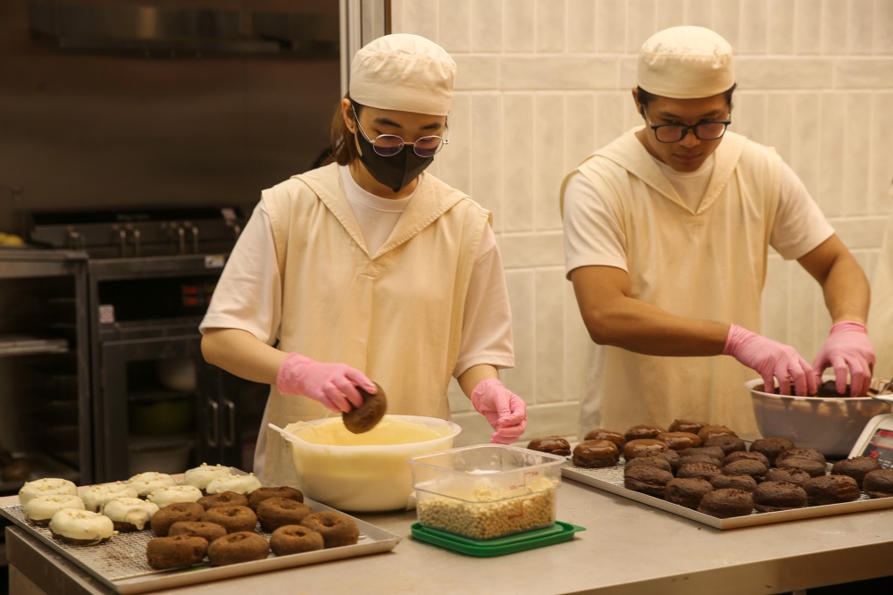 The open kitchen behind orange coloured glass is a hive of activity as everyone works hard to prepare the donuts, such as dipping them in chocolate. — Picture by Choo Choy May