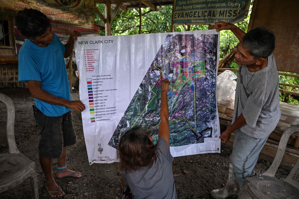 Residents looking at a map with proposed projects by the Bases Conversion and Development Authority (BCDA) in Capas. — AFP pic