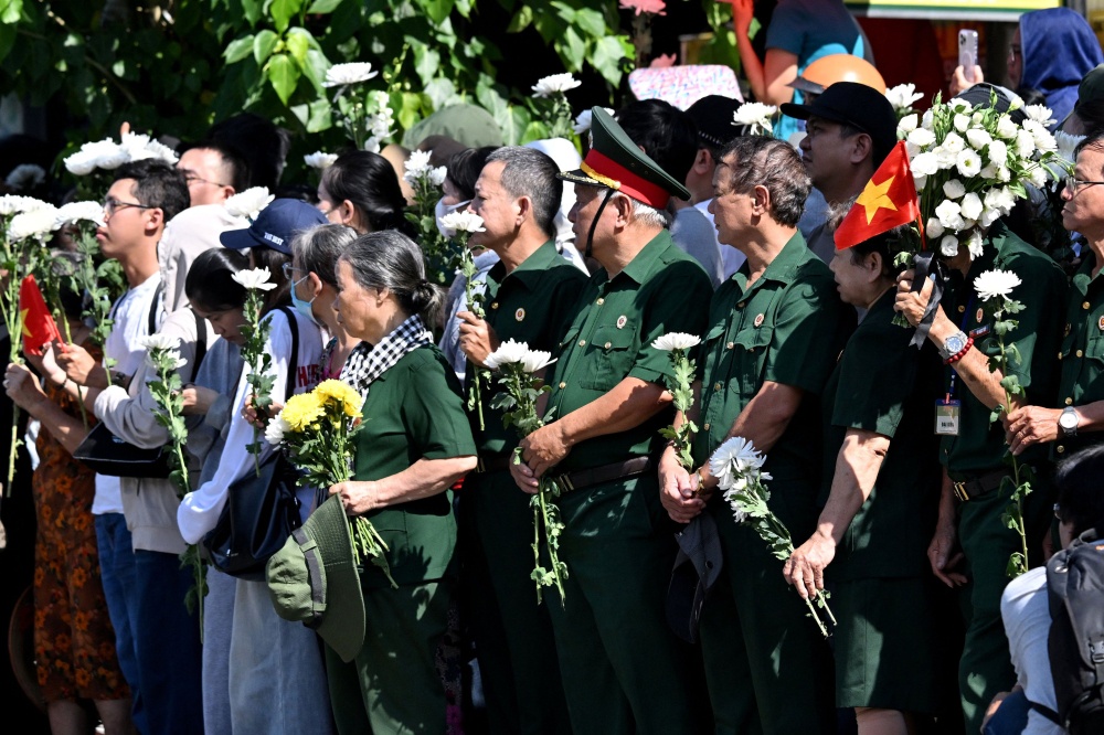People gather with flowers by a roadside as they wait for the vehicle transporting the remains of fallen soldiers to pass by in Ho Chi Minh City October 14, 2026. — AFP pic